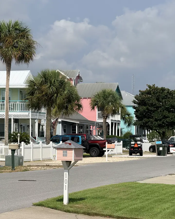 Pastel cottages with metal roofs and picket fences along a palm-lined street in Bid-A-Wee, Panama City Beach.