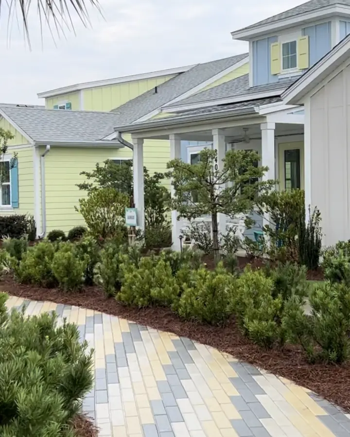 Pale yellow cottage with a covered front porch and dormer, fronted by shrub beds and a paver walkway at Latitude Margaritaville, Panama City Beach.