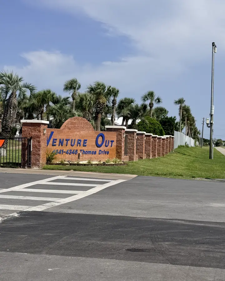 Brick-and-stucco Venture Out entrance sign on Thomas Drive framed by palms, Panama City Beach.